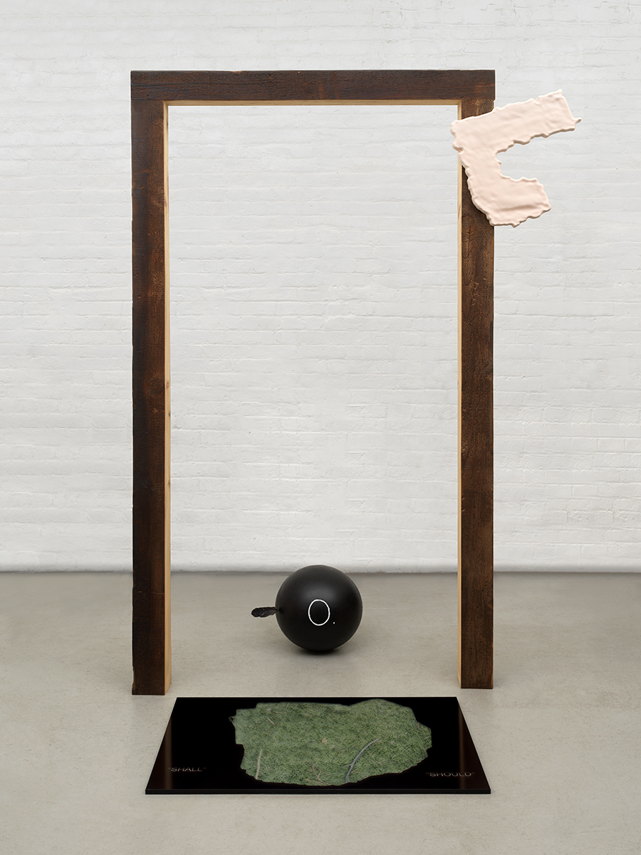 Sculpture of free-standing wooden frame, attached HDU foam object, and steel ball with feather and vinyl print on acrylic on floor